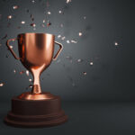A bronze trophy cup with confetti on a dark background