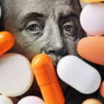Money and healthcare policy concept. Colorful medical pills cover Benjamin Franklin's face on one hundred american dollar bill. Macro top down view.