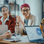 Group of diverse workers collaborate around a table looking at graphs on a laptop