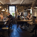 A wide angle view of a group of diners in their friendship groups enjoying a meal in a warm coastal pub in Seahouses in the North East of England. They are sat inside the warm glass conservatory area of the pub in the dining area and enjoying some rustic food and drink