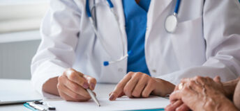 Midsection of female doctor sitting at the desk in an office and discussing test results with senior woman. Close up of hands, unrecognizable people.