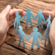 Cropped image of businessman's hands covering paper team on wooden table