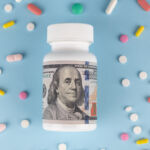 A bottle of pills with a dollar bill wrapped around it on a blue background with drugs scattered around it